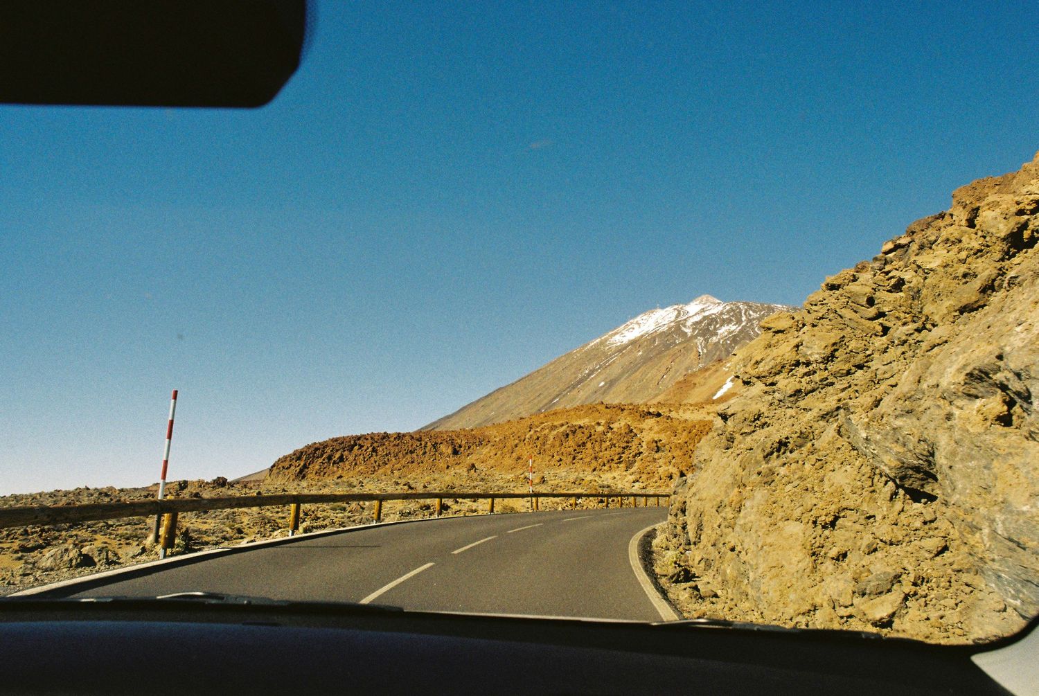 A scenic mountain road curves through rocky terrain with snow-capped peaks visible in the distance.