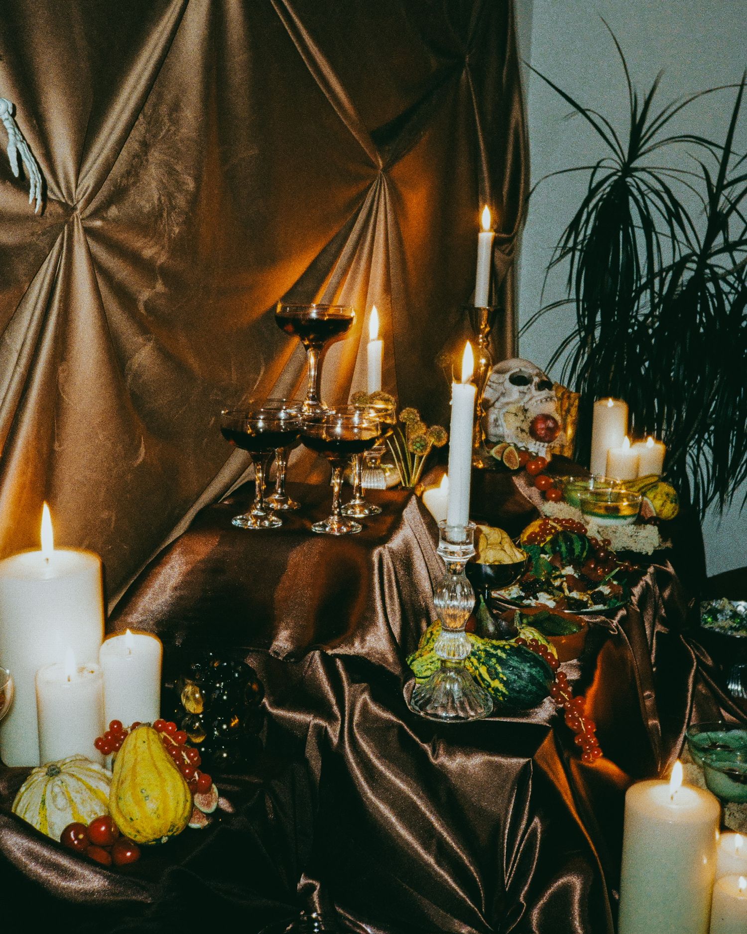 Halloween table display with candles, pumpkins, and decorative elements against brown fabric backdrop.