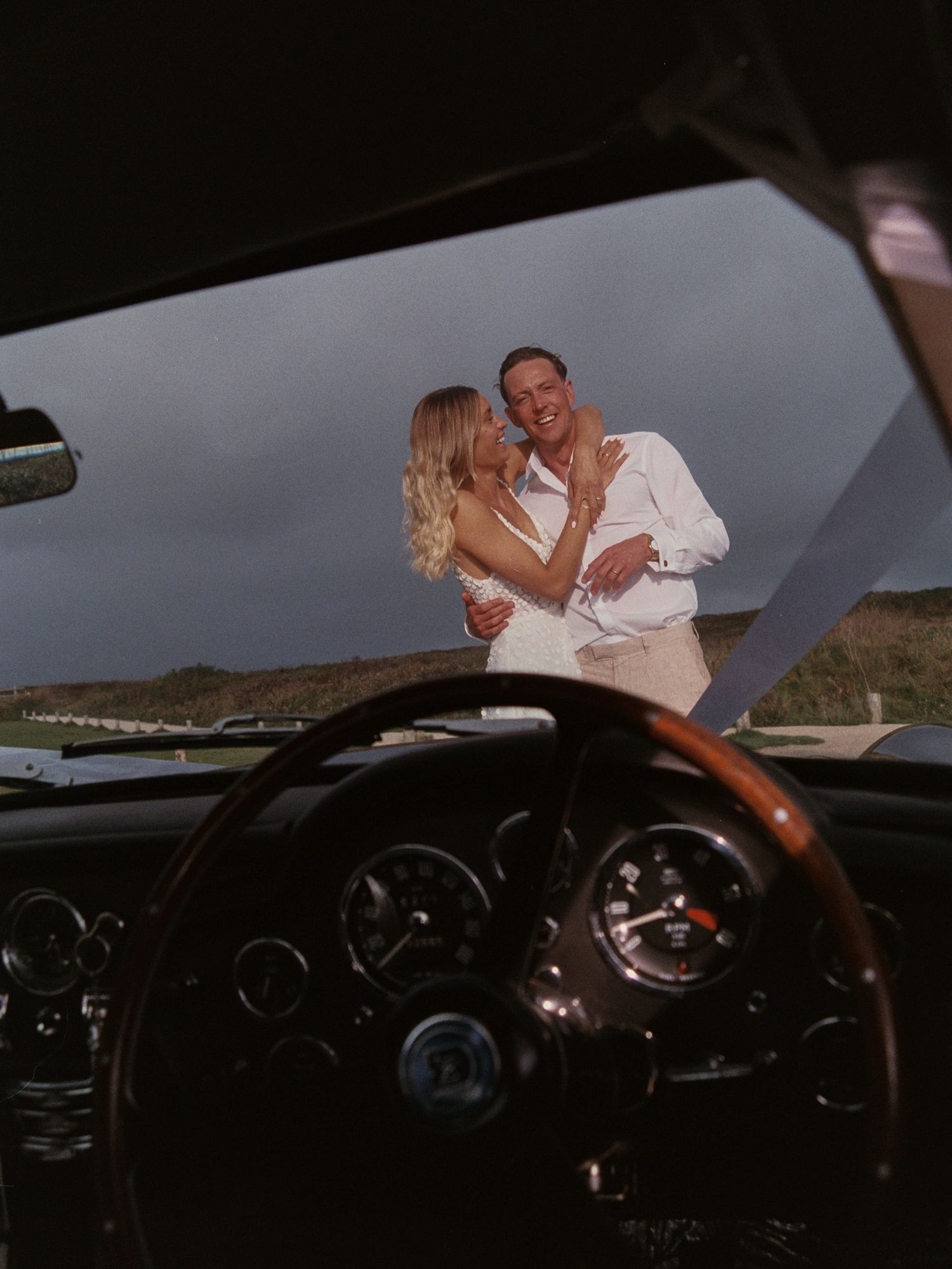 A romantic moment captured through a car windshield during sunset.