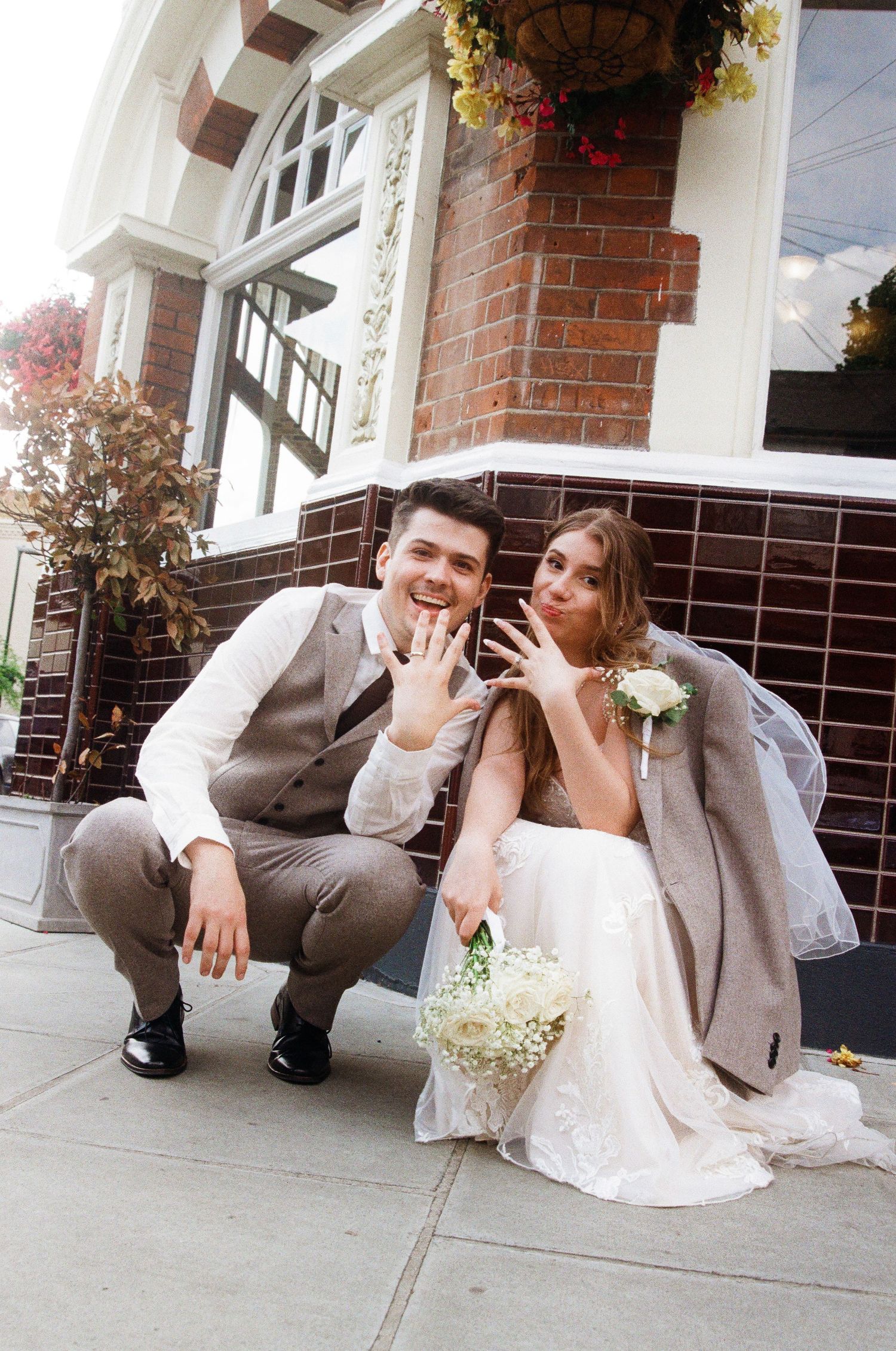 Casual wedding portraits taken outside a historic brick building with decorative trim.
