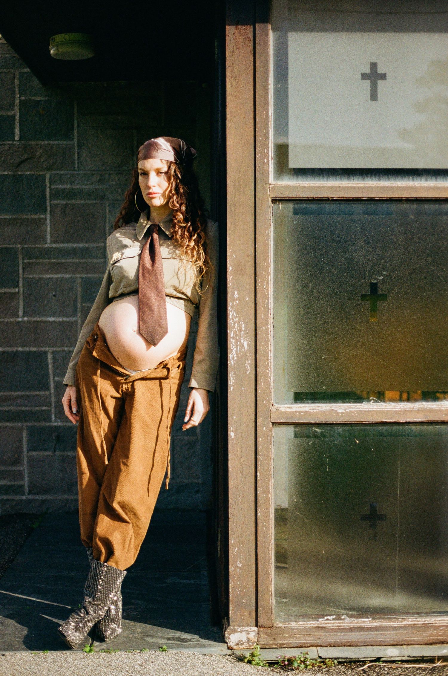 Artistic maternity portraits in a brown coat against a shadowy doorway.