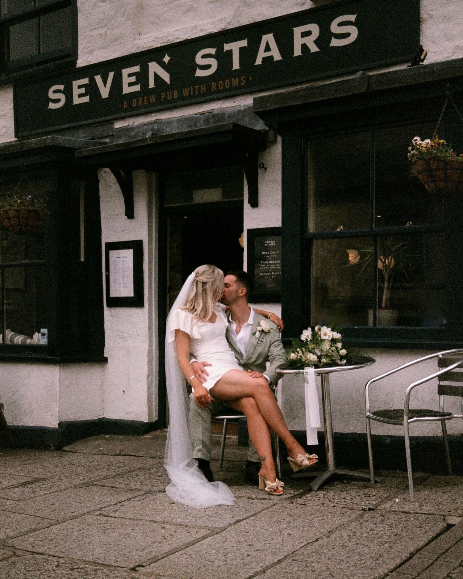 A couple in wedding attire sits outside Seven Stars establishment.