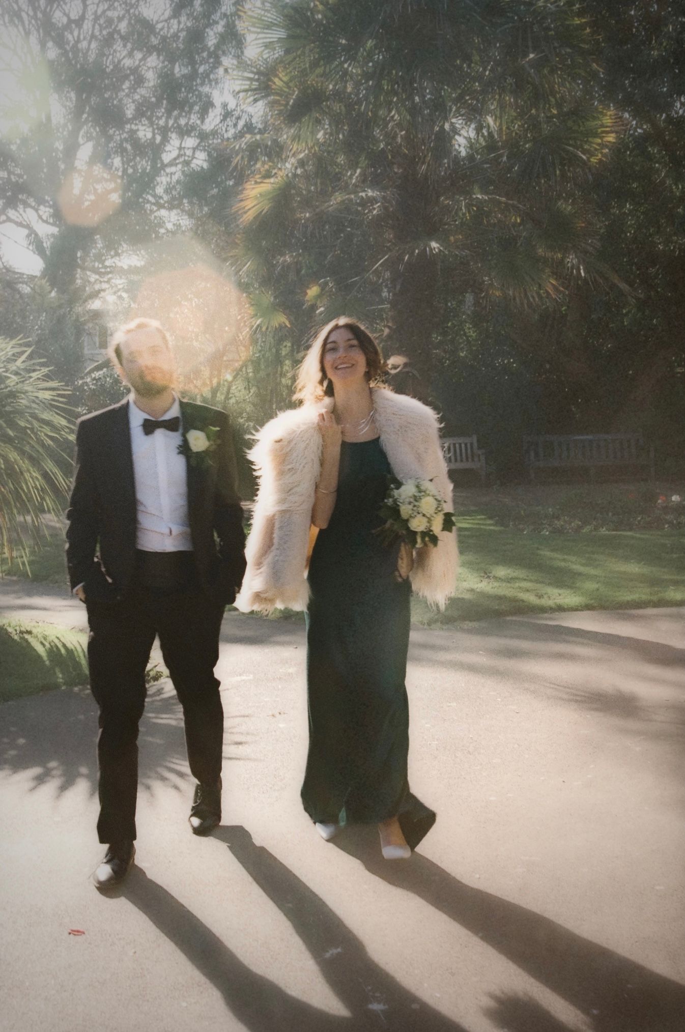 Wedding party casts long shadows while walking on sunlit pathway.