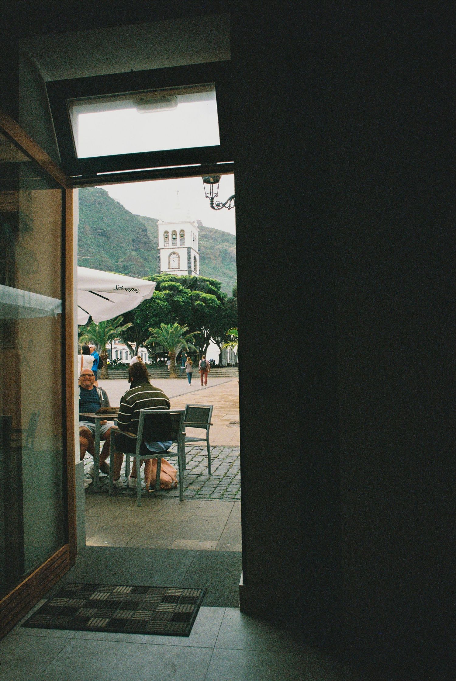 Dark interior view looking out through doorway to outdoor plaza area.