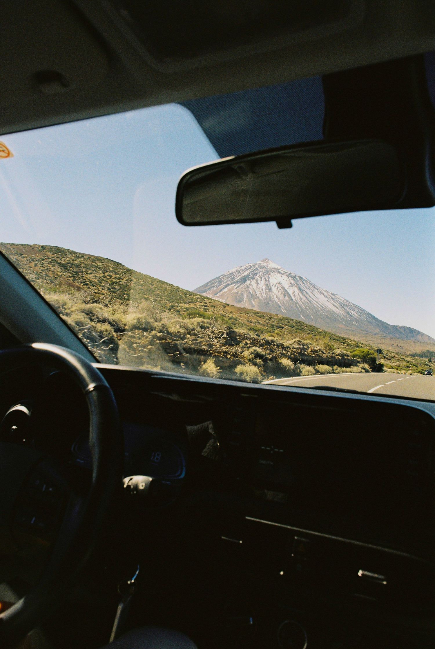 Scenic mountain view through car windshield while driving on winding desert road.
