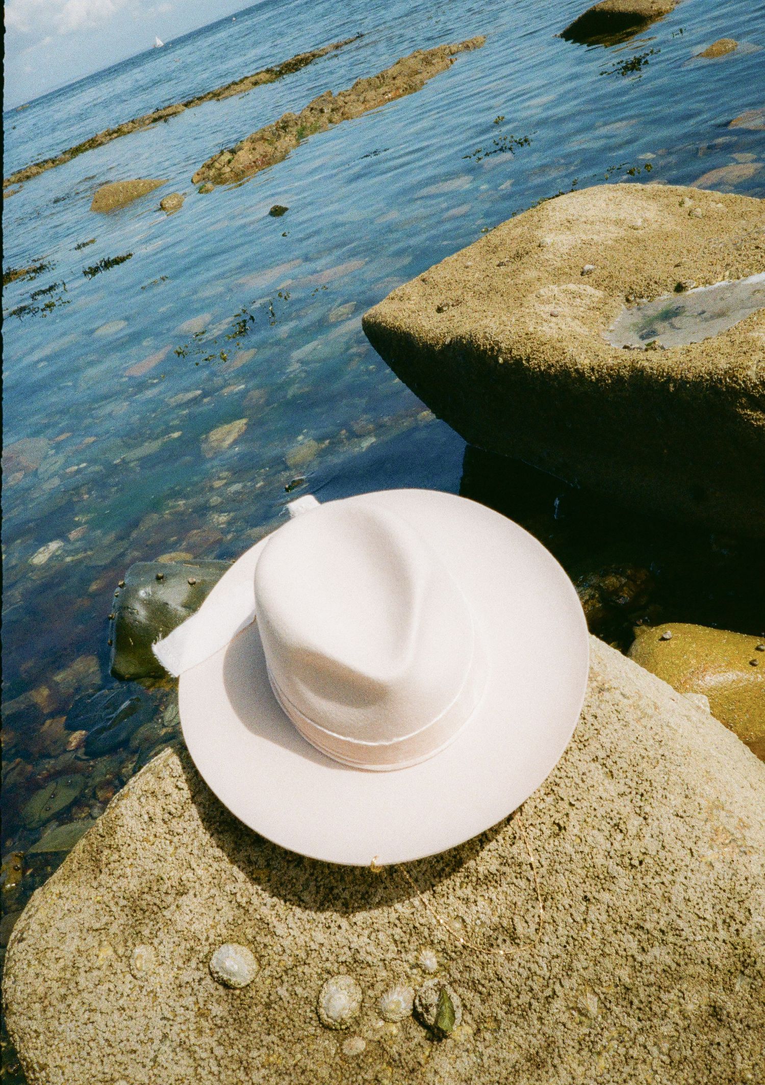 White wide-brimmed hat photographed on coastal rocks with ocean waves in background.