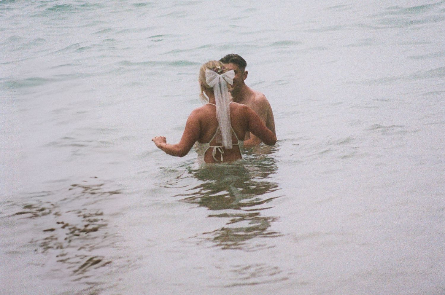 People wading and swimming in gentle ocean waves on a cloudy day.