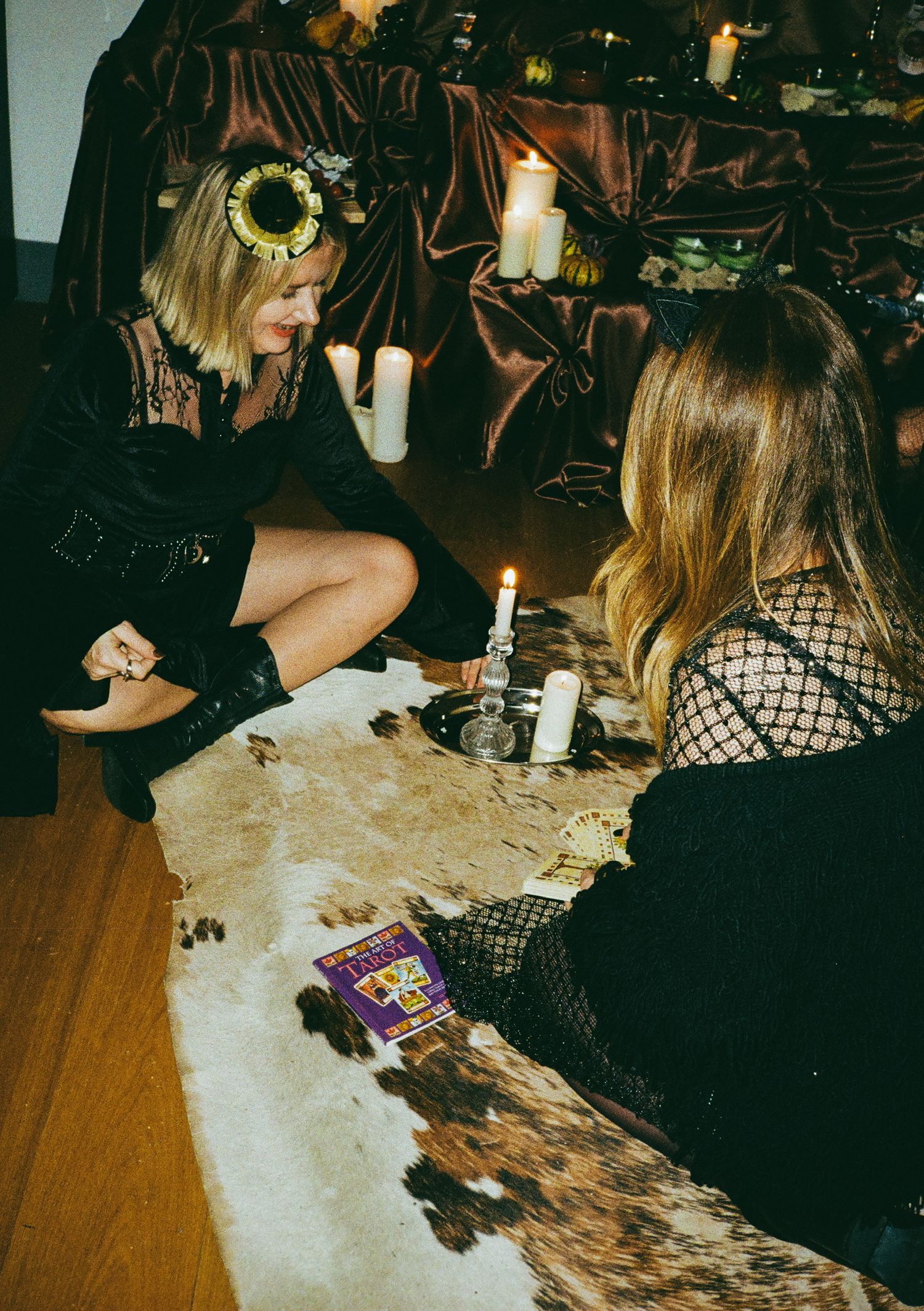 Group gathered around a candlelit table playing cards at a Halloween party.