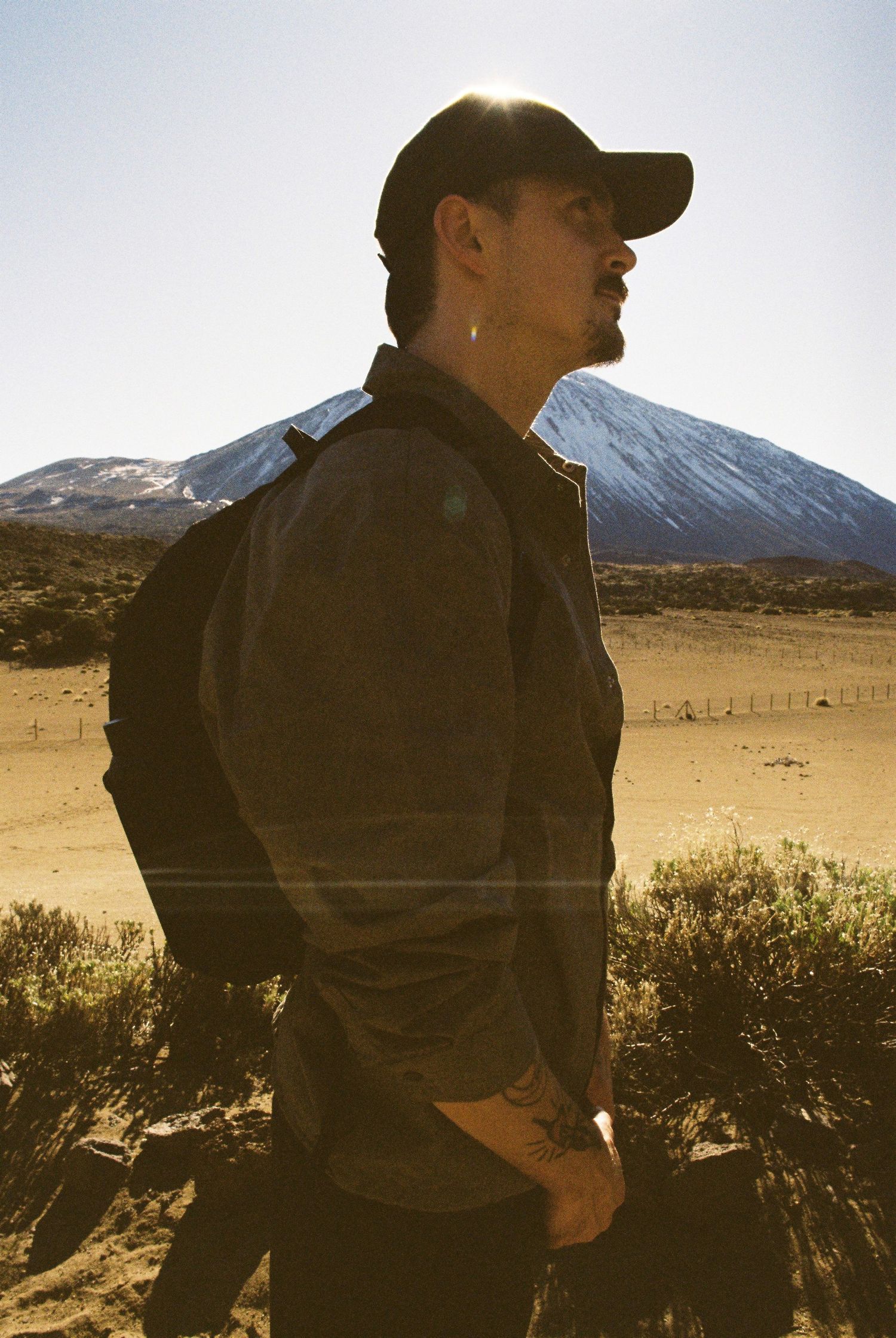 Silhouetted figure stands in desert landscape with snow-capped mountain in background.