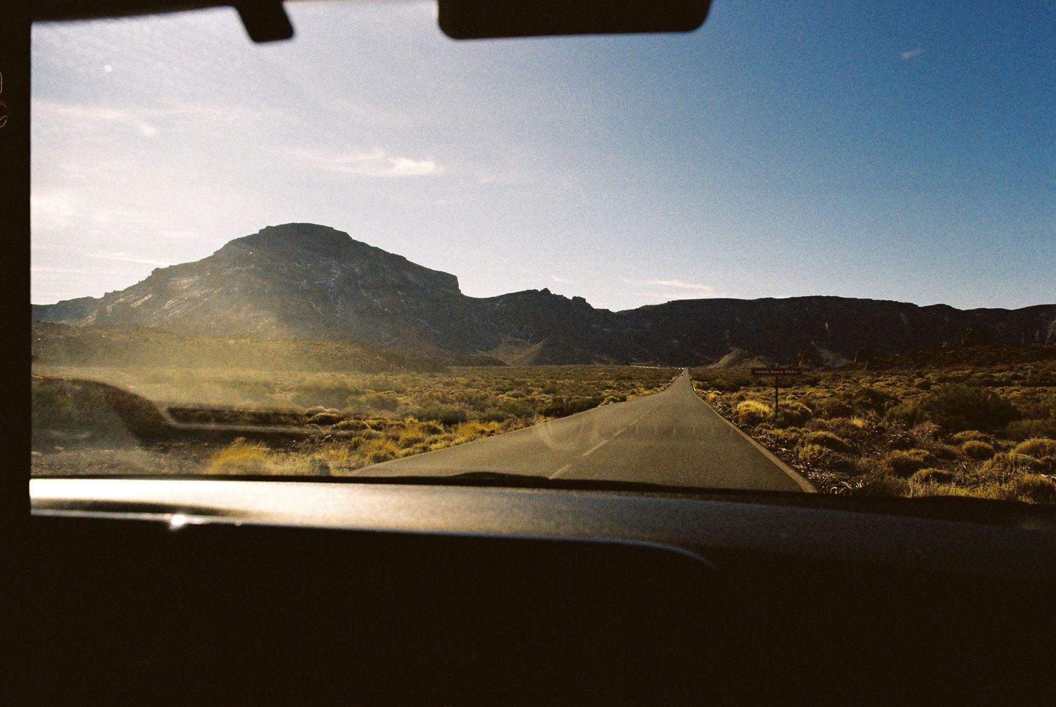 Panoramic desert landscape with winding road and mountains under bright sunlight.