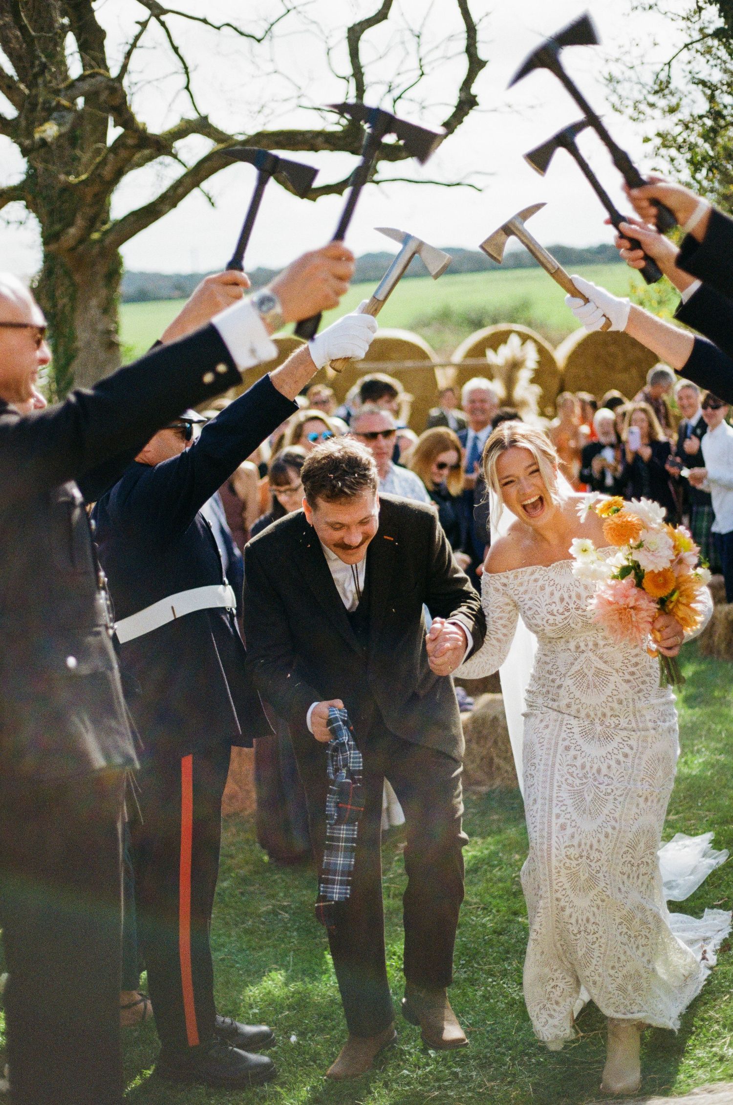 Bride and groom walk under an arch of raised axes during their outdoor wedding ceremony exit.