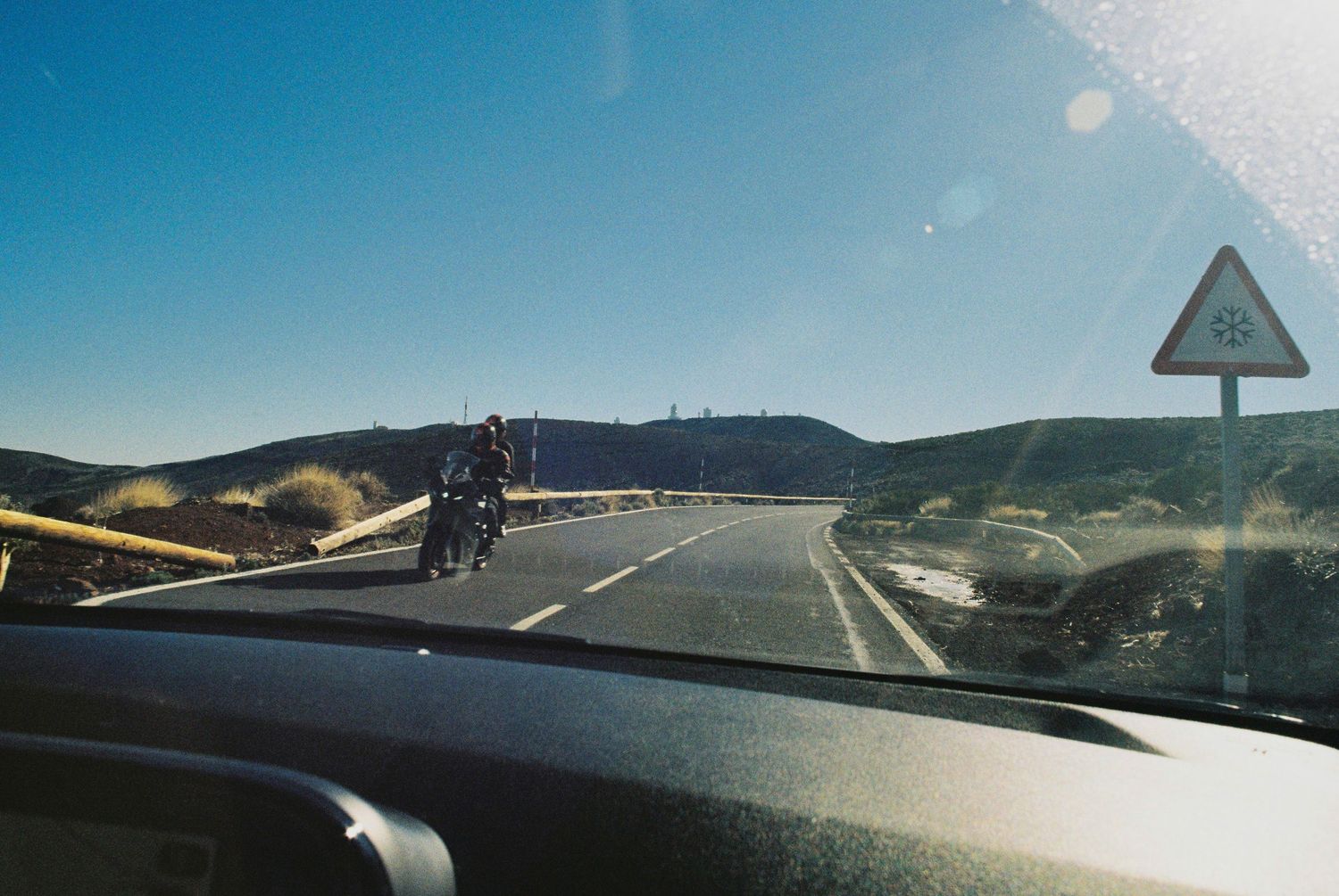 Desert highway stretching into distance with mountains on horizon under blue sky.
