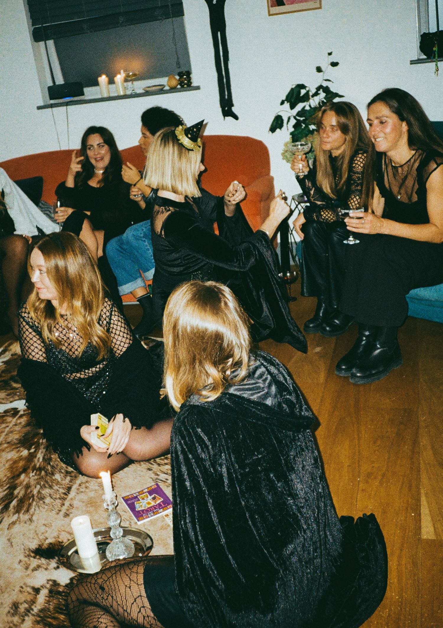 A group gathers in a room decorated with dark fabrics and candles for a Halloween-themed party.