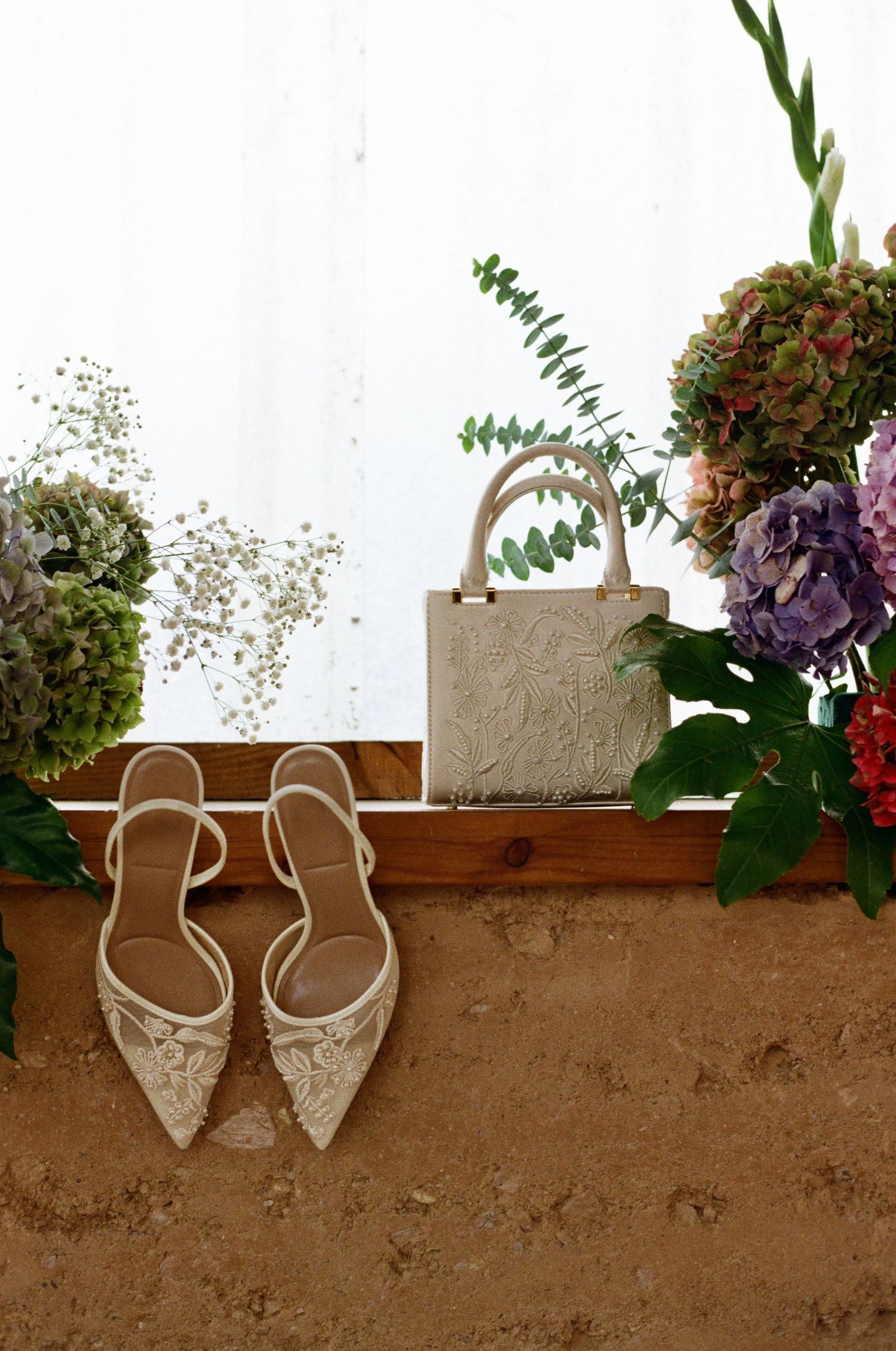 Elegant bridal shoes displayed on a rustic wooden ledge with floral decorations.