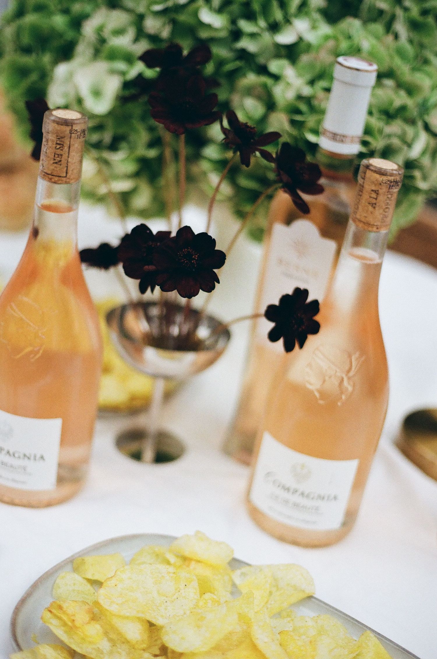 Bottles of rosé wine and potato chips arranged on a white tablecloth for a party.
