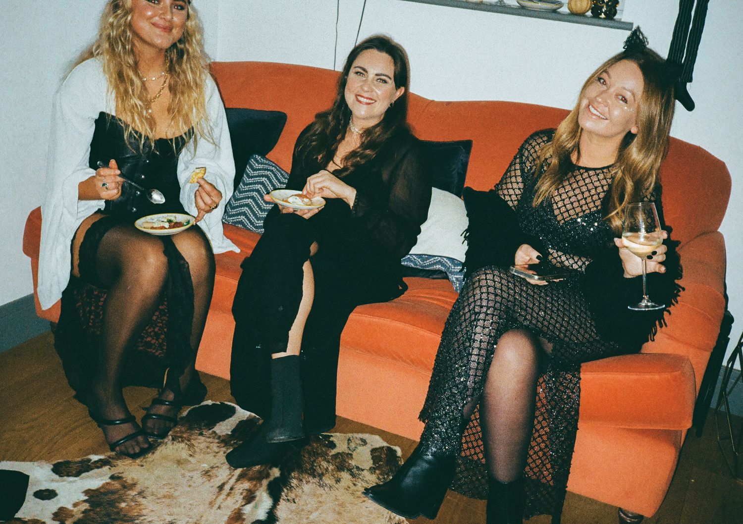 Group relaxing on an orange couch during an evening social gathering.