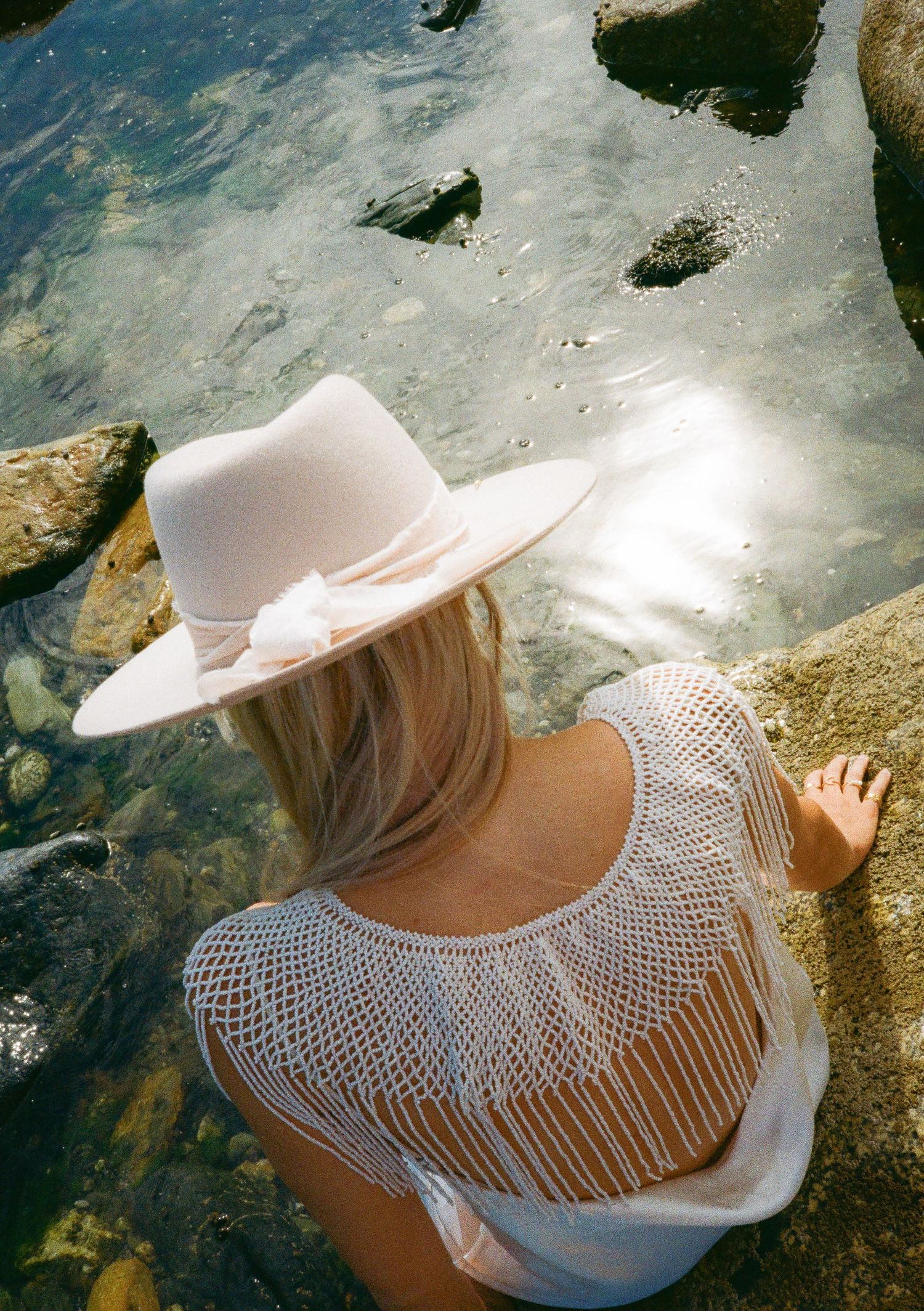 Artistic seaside photo series showing a white sunhat and macrame neckpiece against rocky background.