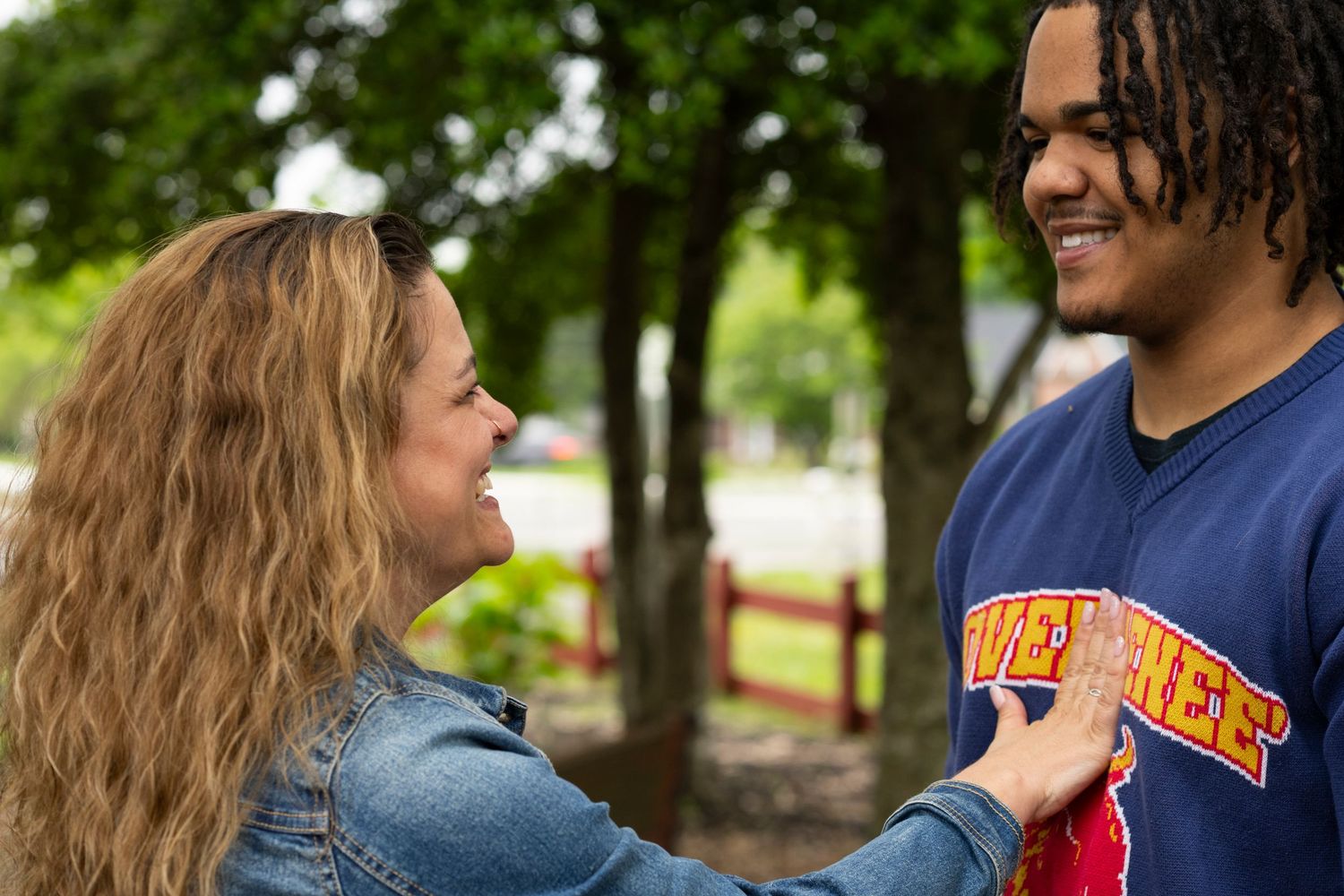 A couple shares a tender moment while walking together through a lush green park on a sunny day.