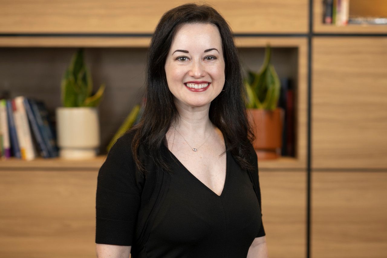 Professional headshot of person in black top against wooden wall background.