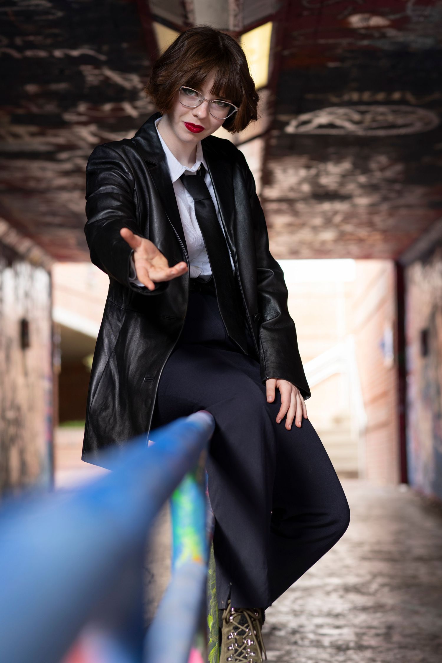 A person in a black leather jacket poses against an industrial backdrop with dramatic lighting.