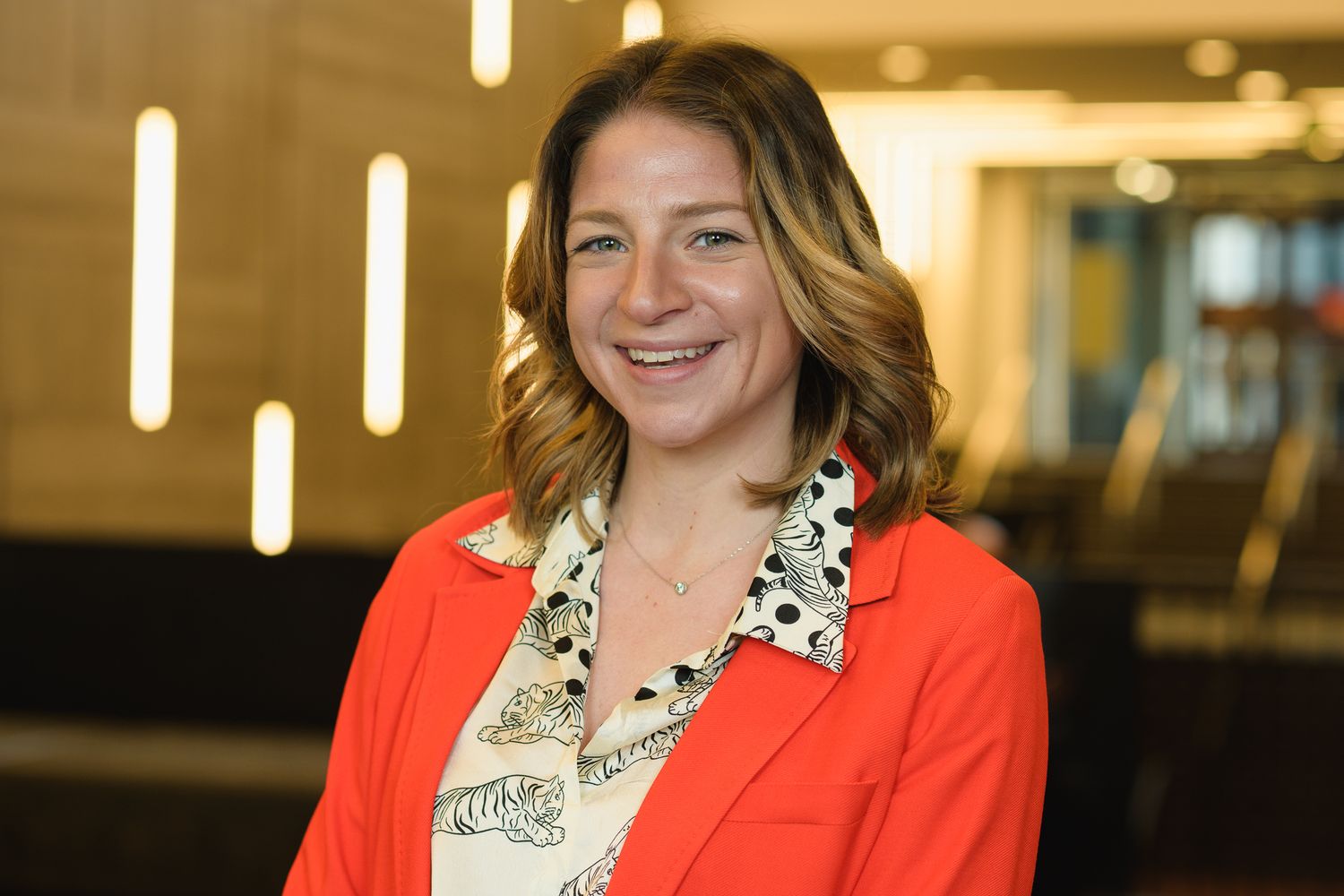 Person wearing a bright red blazer and patterned top smiling at the camera.