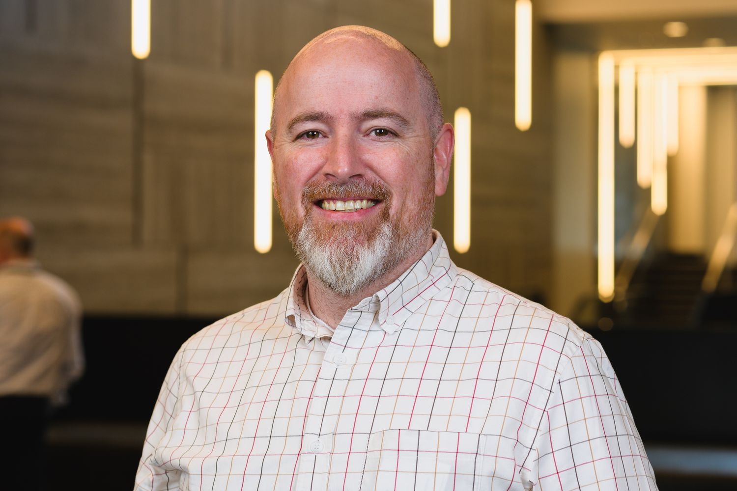 Professional portrait of person in white collared shirt against modern office setting.