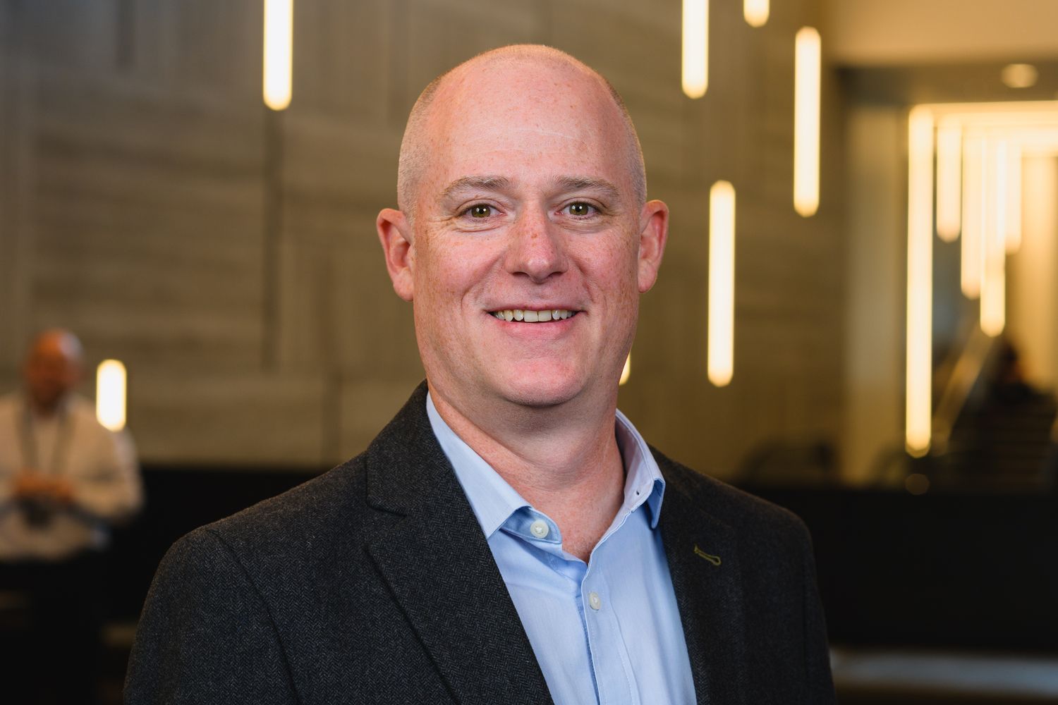 Professional portrait of person in blue shirt smiling against modern office interior.