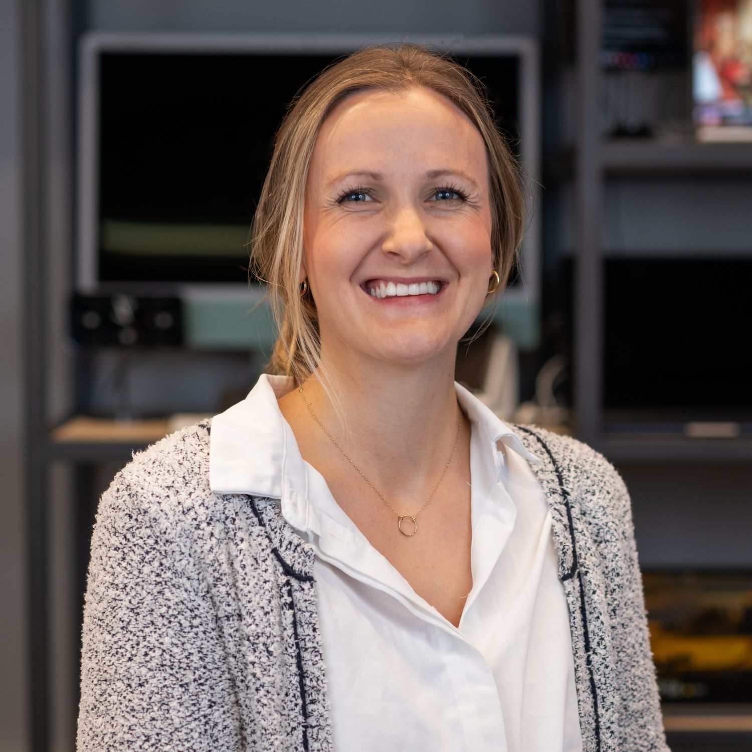 Business portrait of person wearing white shirt and textured gray blazer in office environment.