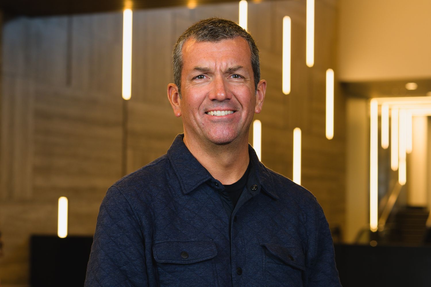 Corporate portrait featuring a person in dark business attire with vertical lighting elements.