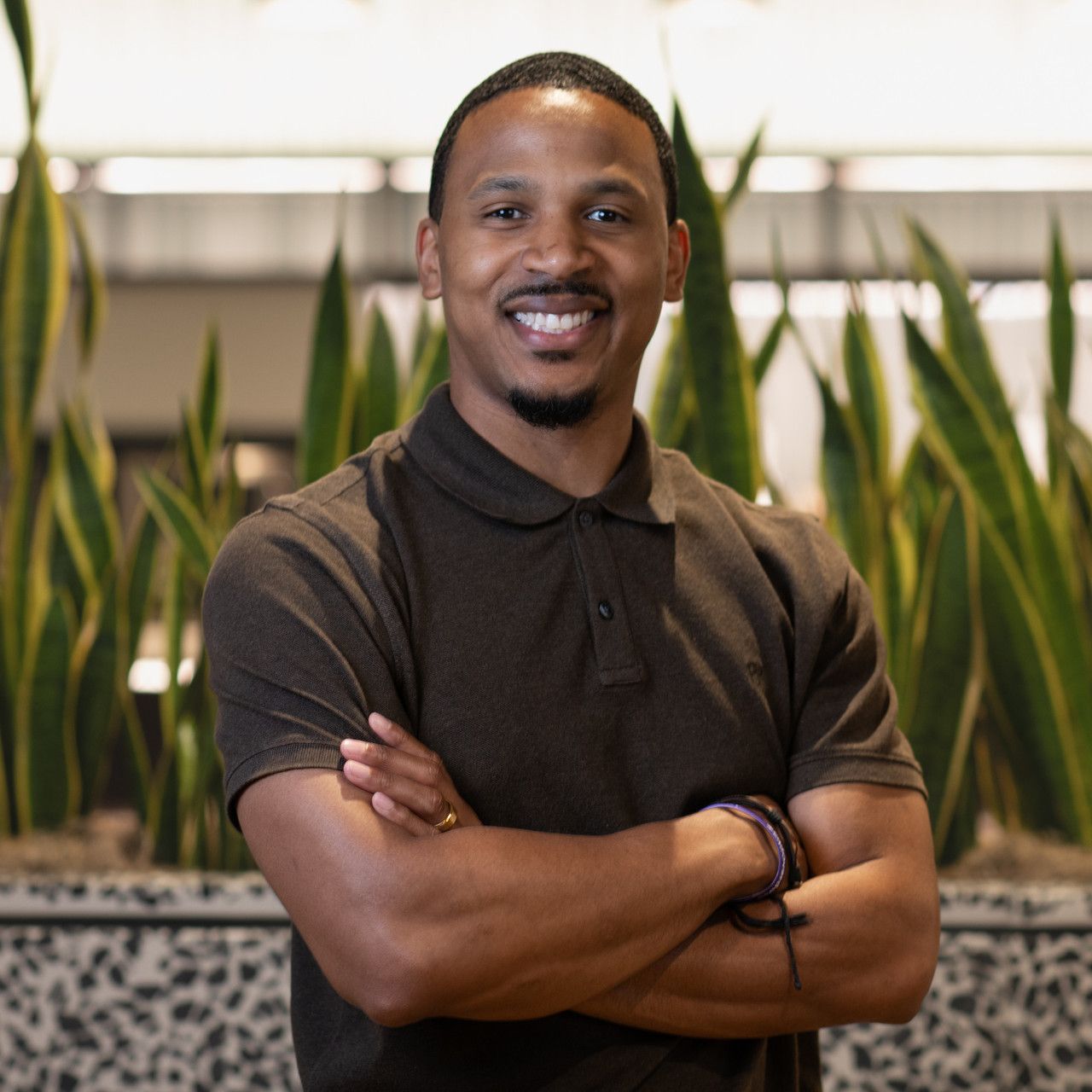 Professional portrait in black attire with indoor plants in background.