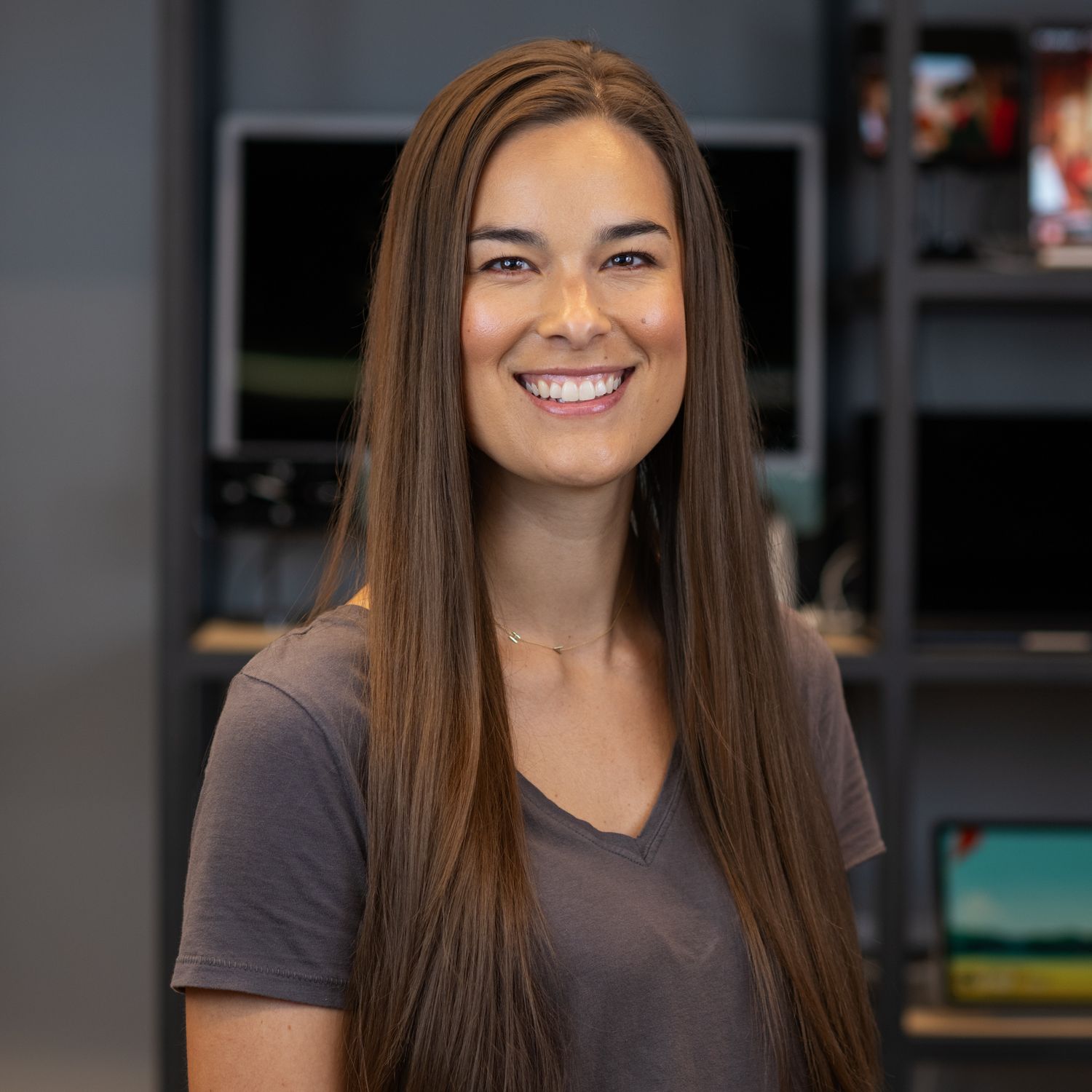 Portrait of person in gray top with long brown hair against dark office background.