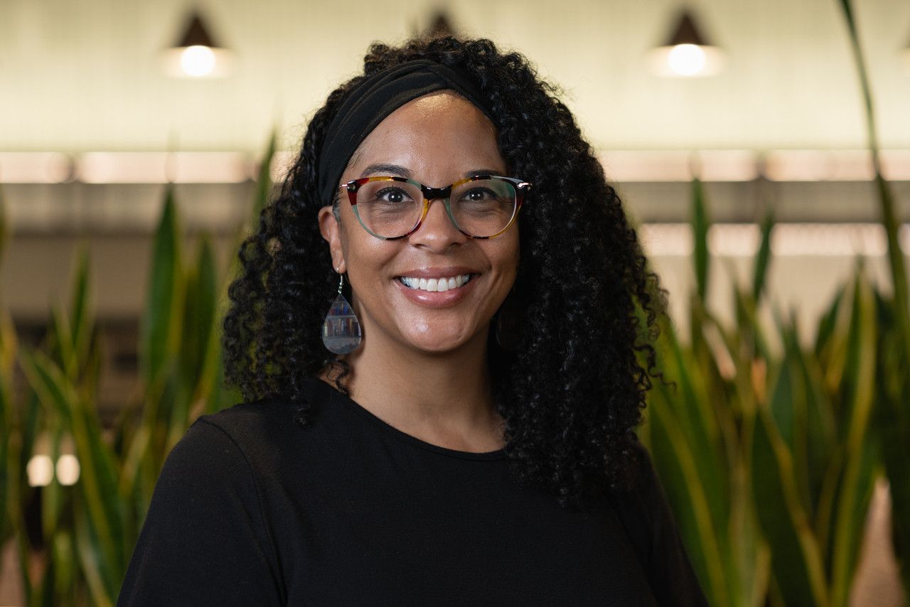 Professional portrait of person with curly hair wearing glasses in office setting.