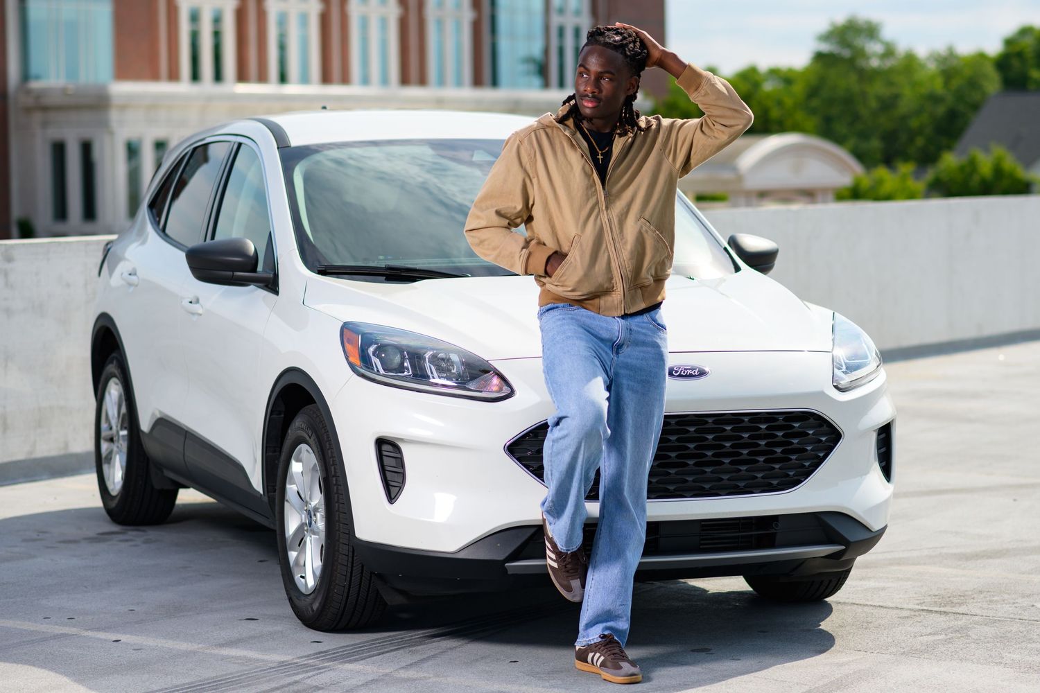 Man in beige jacket and jeans leaning against a white Ford SUV in a parking lot.