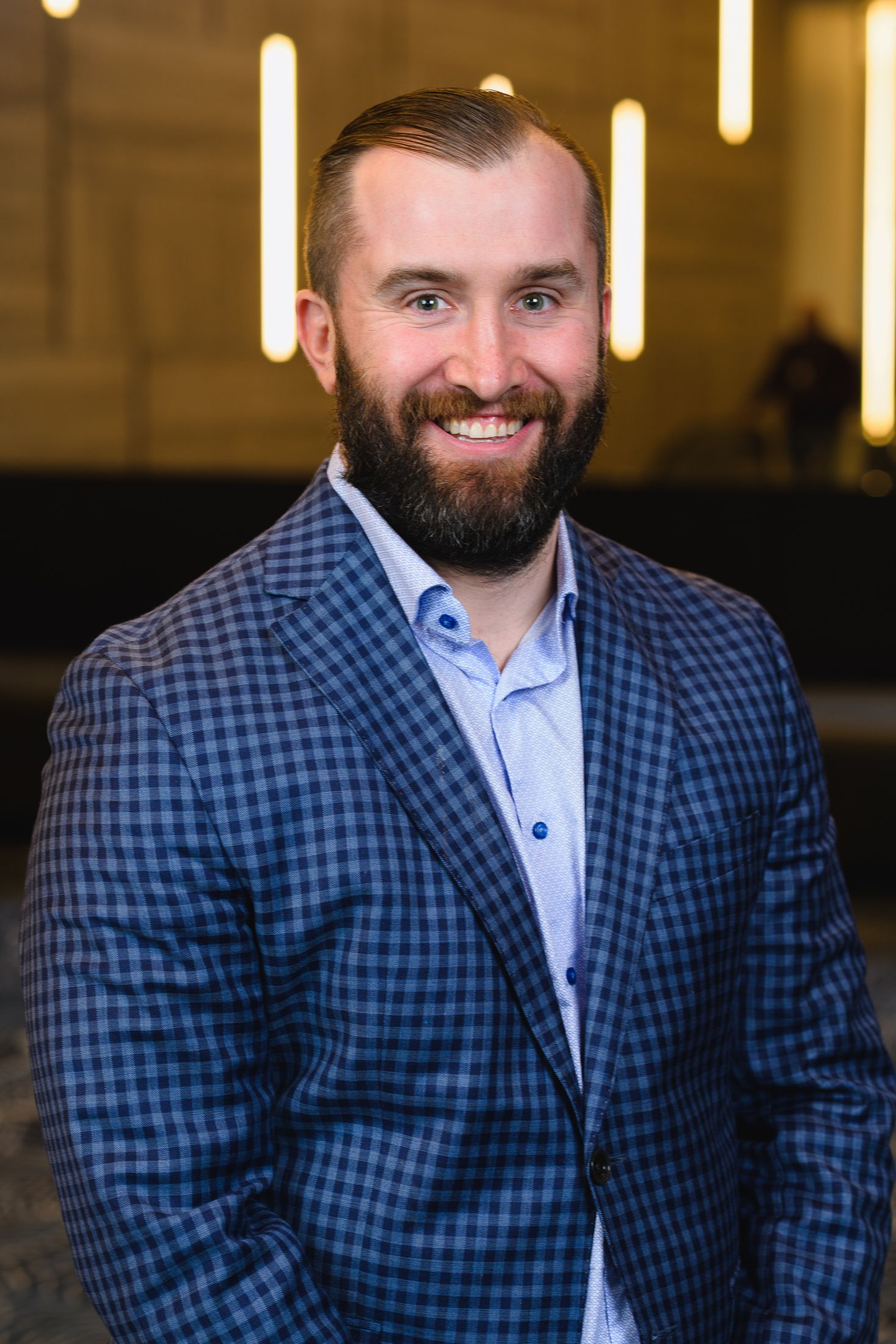 Business headshot of someone wearing a blue checkered suit jacket with light shirt in office setting.