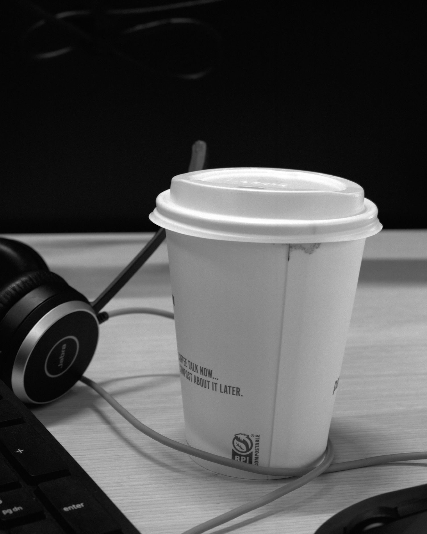 White disposable coffee cups on a desk next to headphones.