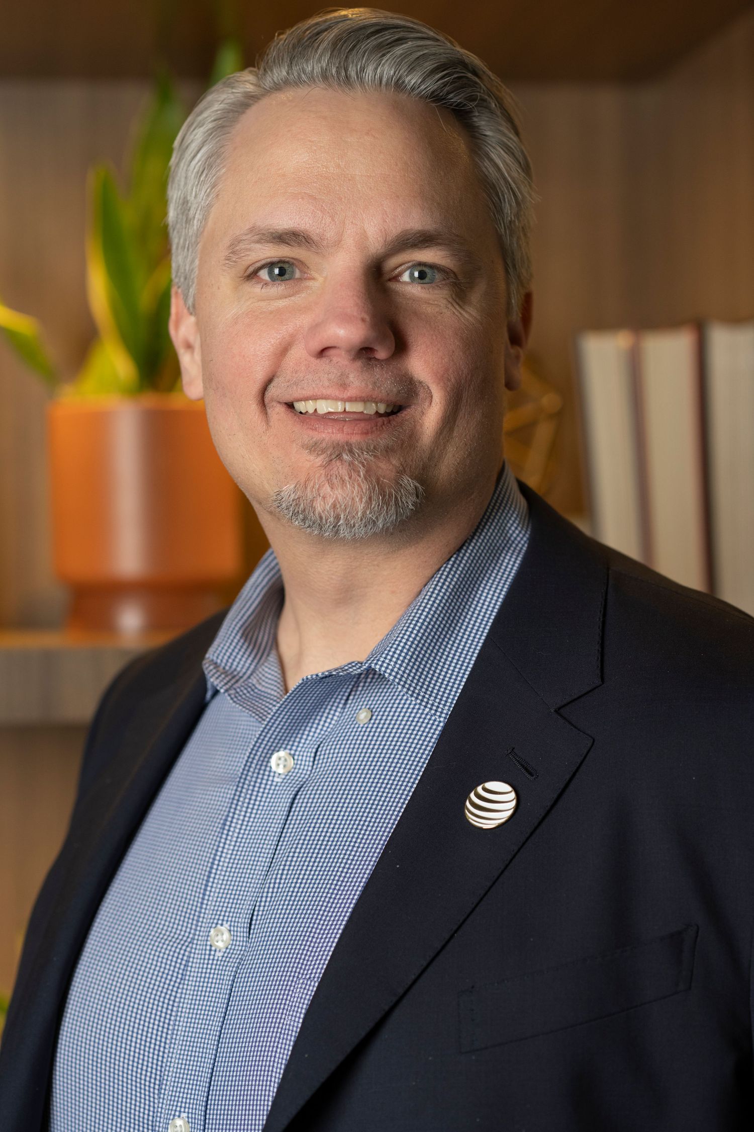 Business portrait of person wearing striped button-down shirt and blazer with AT&T pin in office setting.