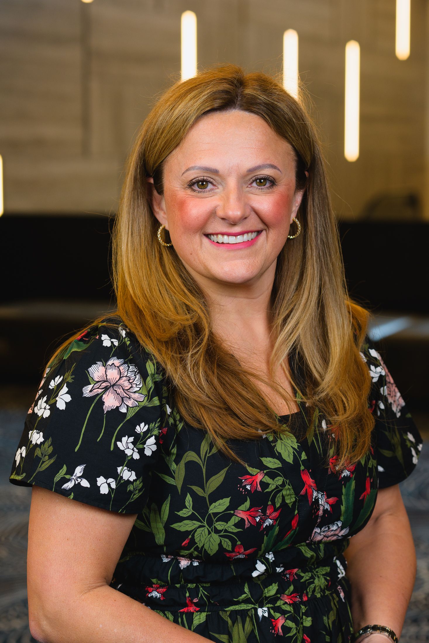 Professional portrait of person in floral dress against modern office setting.
