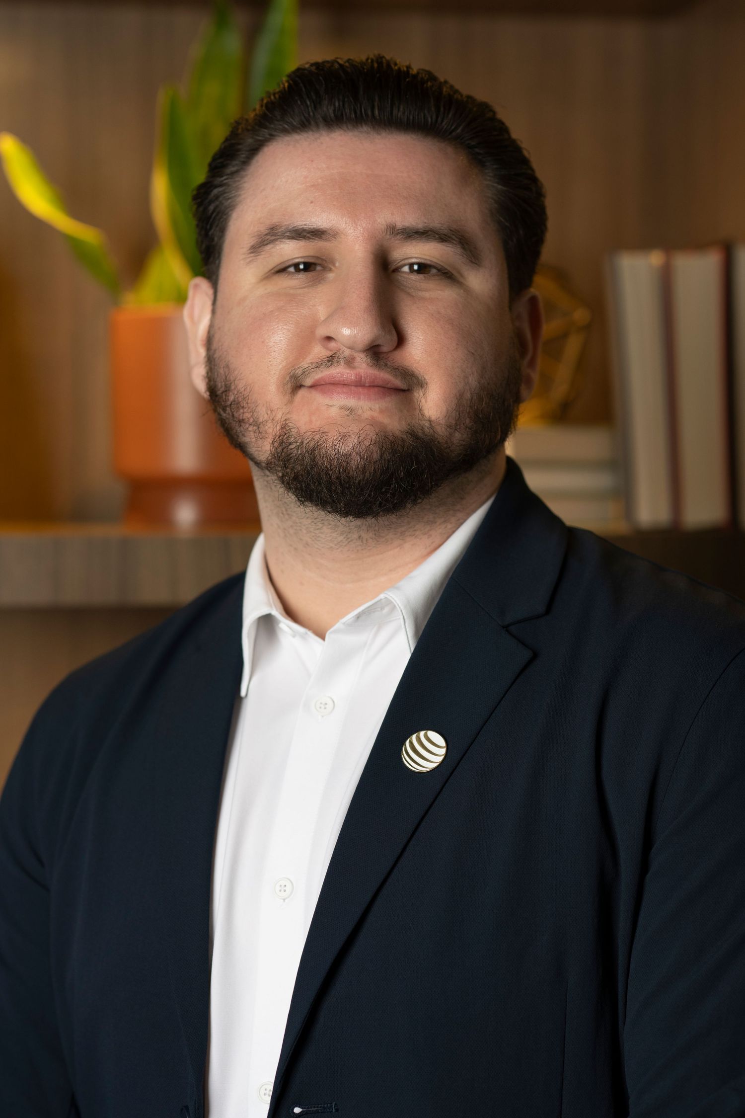 Professional portrait of person in dark suit and white shirt with beard against warm background.