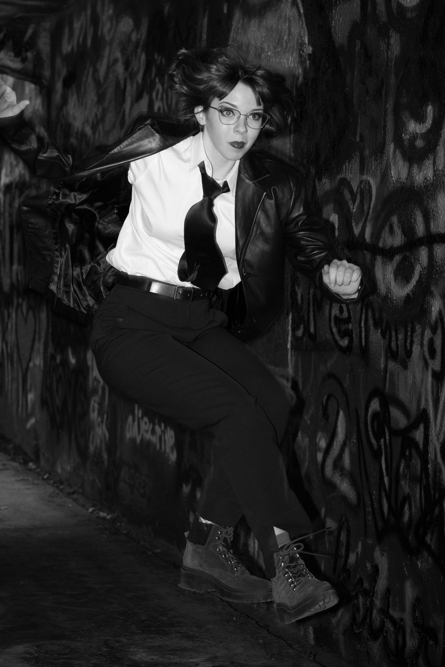 A dramatic black and white photo shows someone in dark clothing leaning against a graffiti-covered wall.