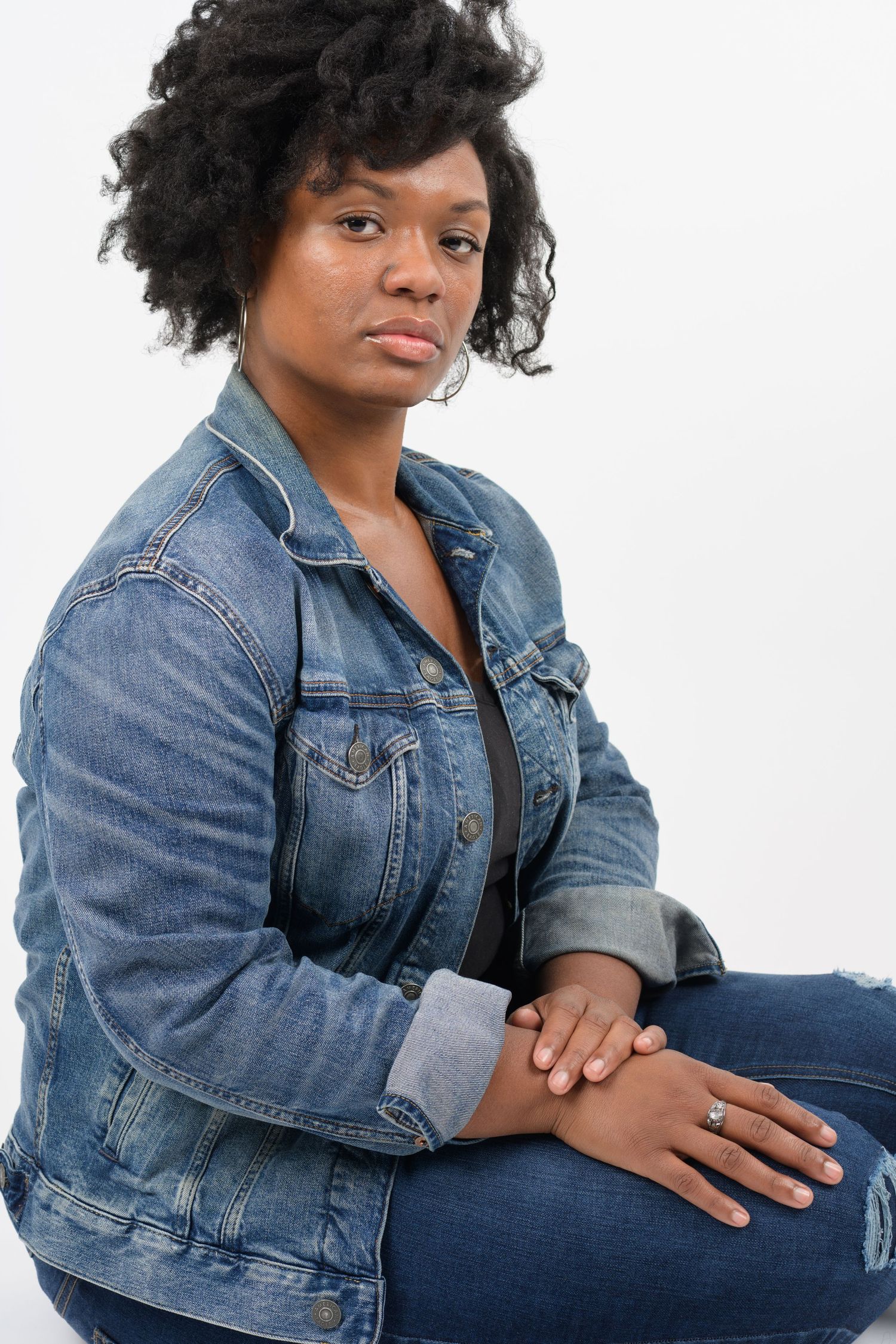 Casual portrait of person in denim jacket sitting against white background.