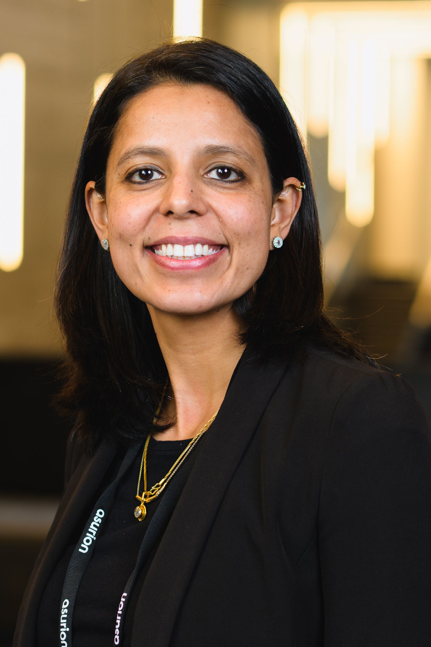 Professional in black blazer shown in warm-lit corporate environment.