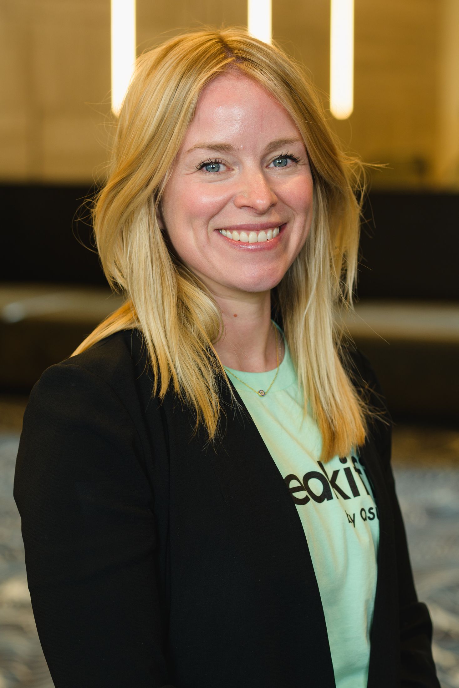 Person in a black blazer and mint green shirt smiling at the camera.