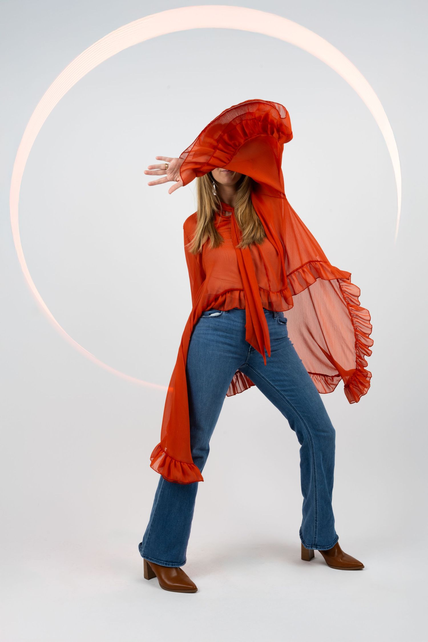 Dynamic pose of person wearing flowing red top and jeans against light studio background.