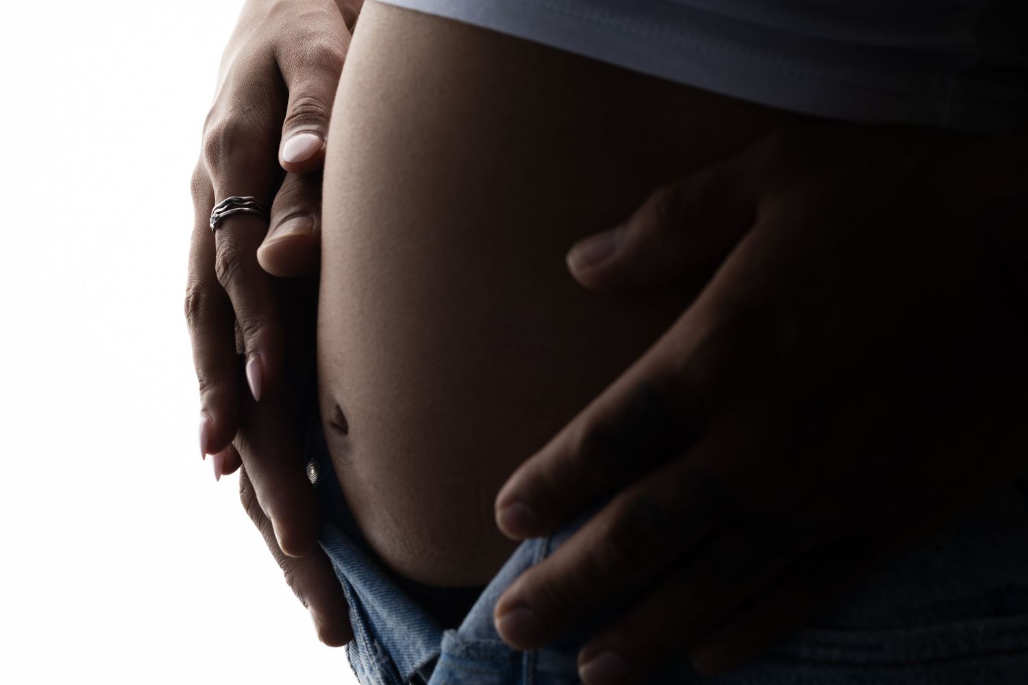 Silhouetted close-up of pregnant belly against dark background.