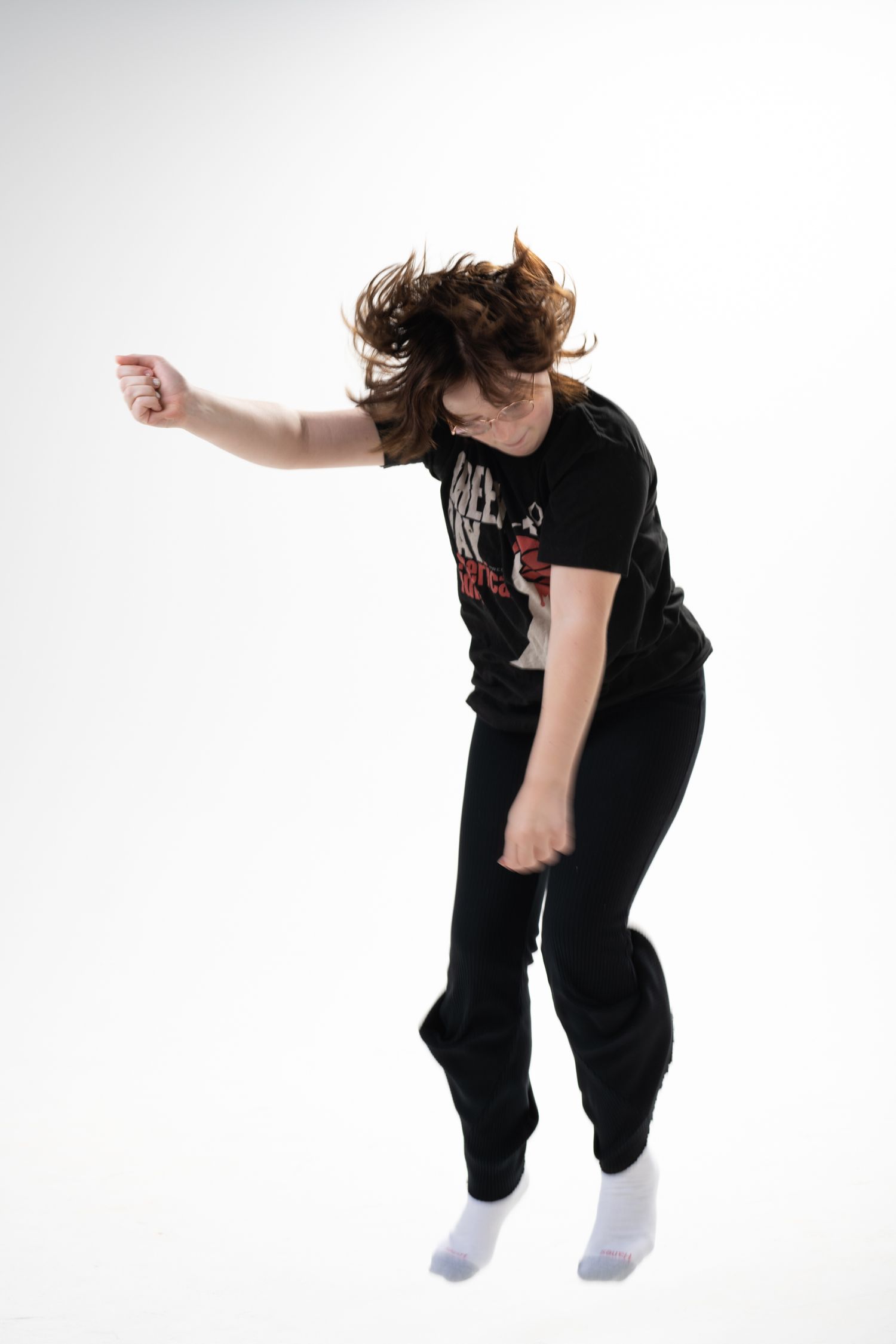 Dynamic shot of someone jumping with hair in motion against white background wearing black clothing.