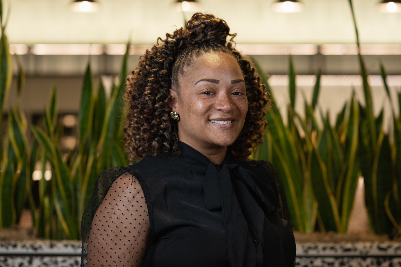 Professional portrait with natural hair and black top against office background.