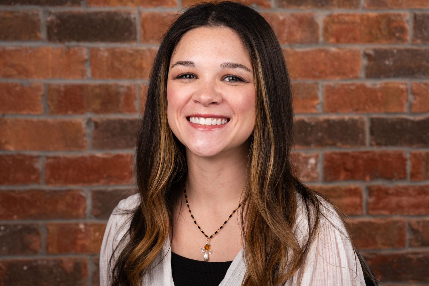 Professional headshot portrait against rustic brick wall background with warm lighting and natural smile.
