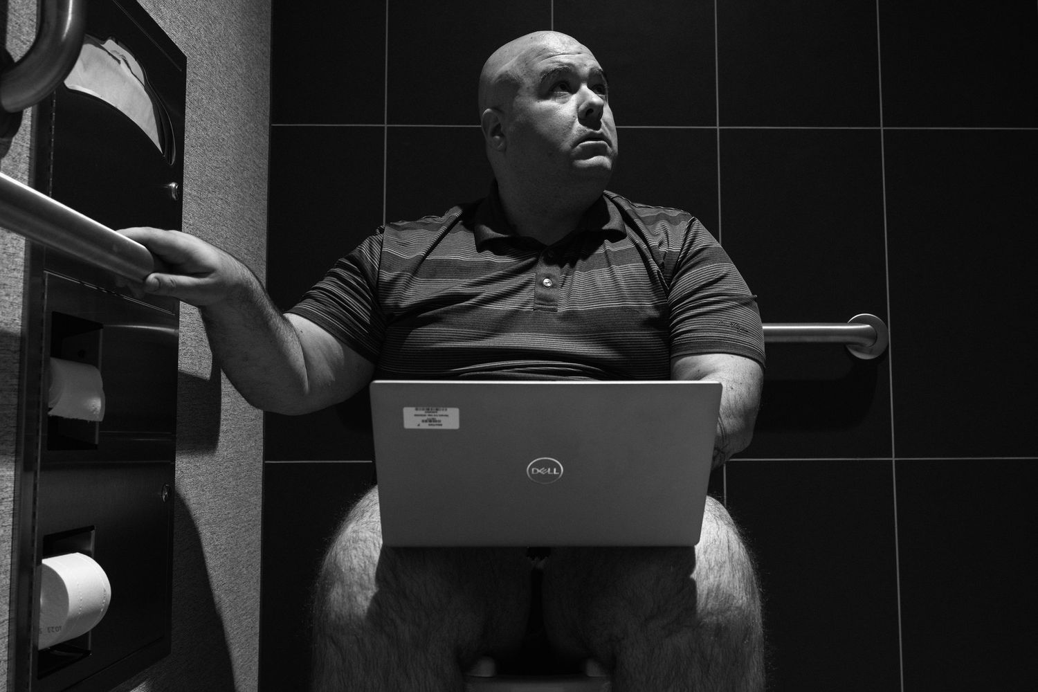 A monochromatic image showing a person sitting in front of a dark tiled wall.