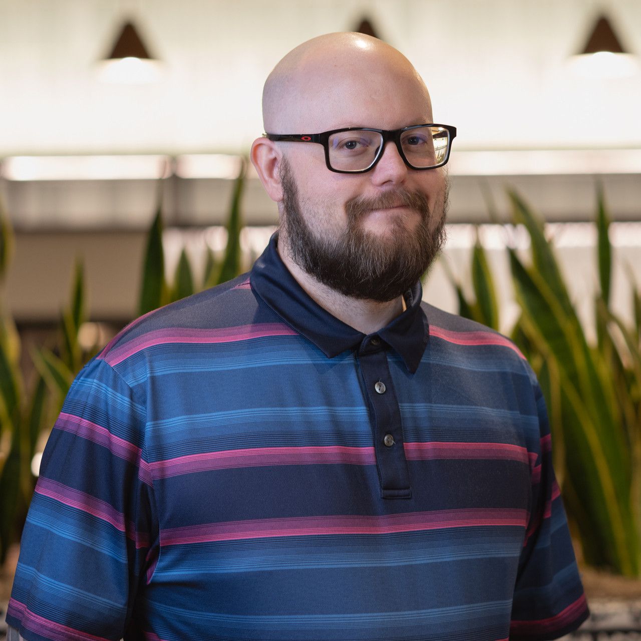 Professional portrait in striped polo shirt with indoor office setting.
