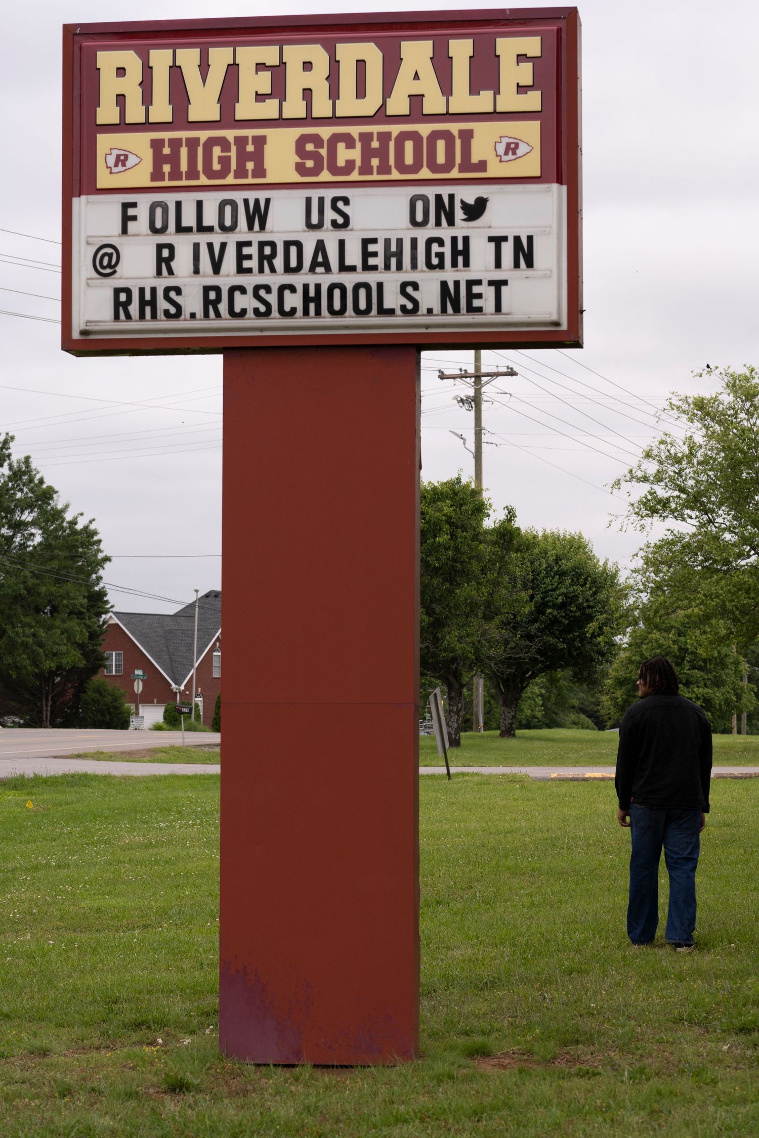 A red sign post displays 'Riverdale High School' with social media information and a person standing in the distance.